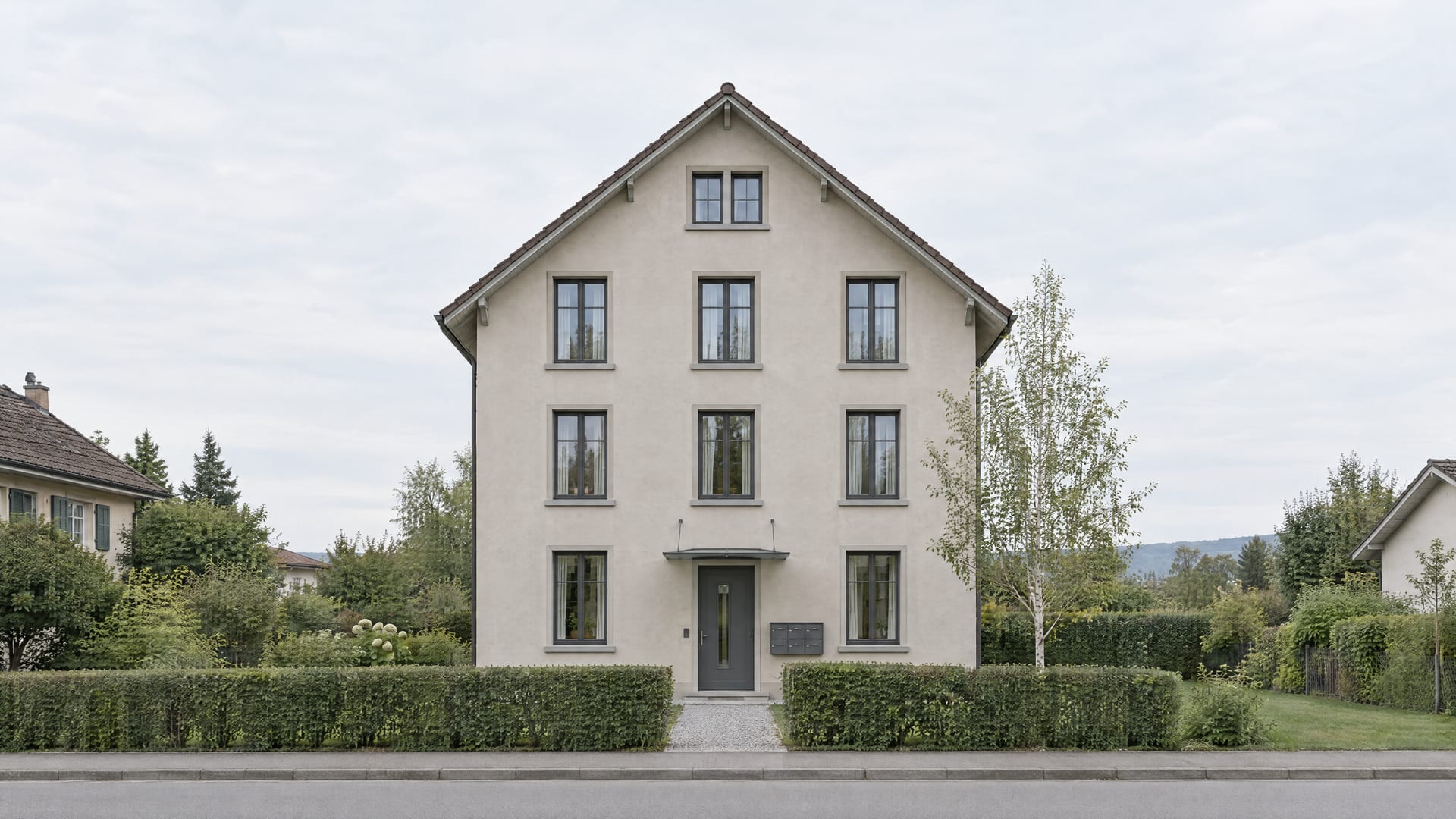 Wohnhaus aus den 1920er Jahren mit steilem Giebeldach, hellem Verputz und Briefkastenanlage beim Eingang